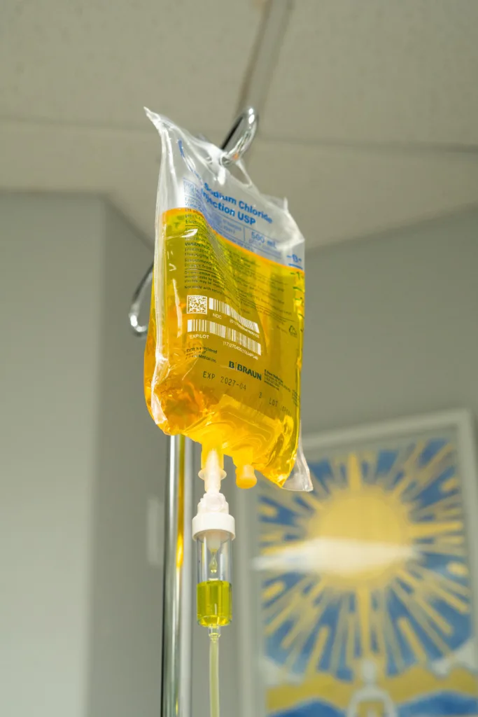 IV bag with yellow liquid, hanging on a metal pole in a hospital room.