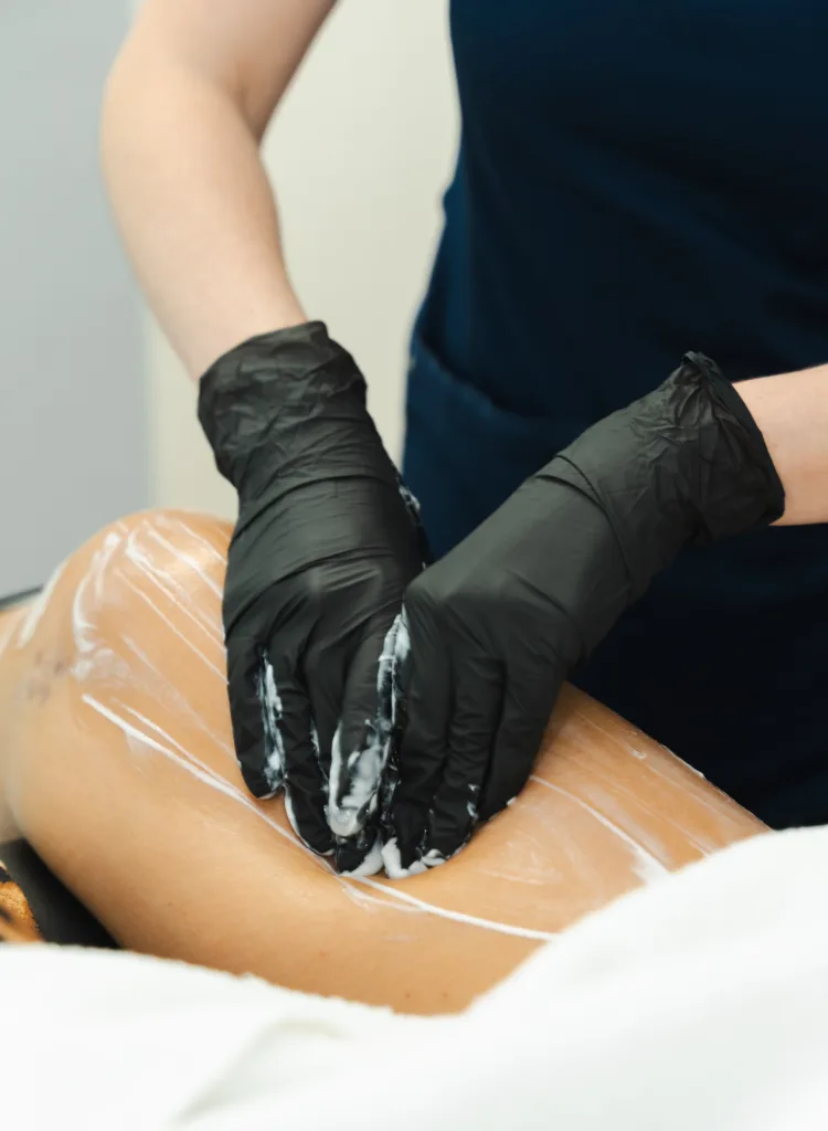 Black gloves apply cream on a person's leg during a massage session.