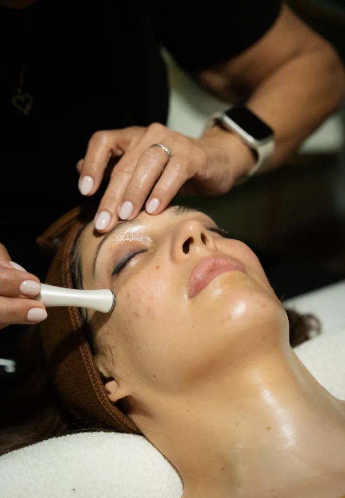 A woman receives a facial treatment with a tool on her cheek.